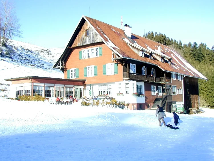 Gasthaus mit Terrasse auf der Personen im Winter an der Sonne sitzen