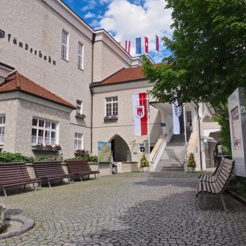 Museumseingang mit Flaggen und Skulptur im Vordergrund.