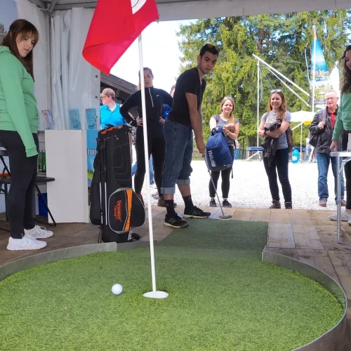 Person spielt Minigolf mit Zuschauern im Zelt.