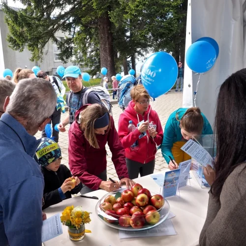 Personen bei einem Informationsstand mit Luftballons und Äpfeln.