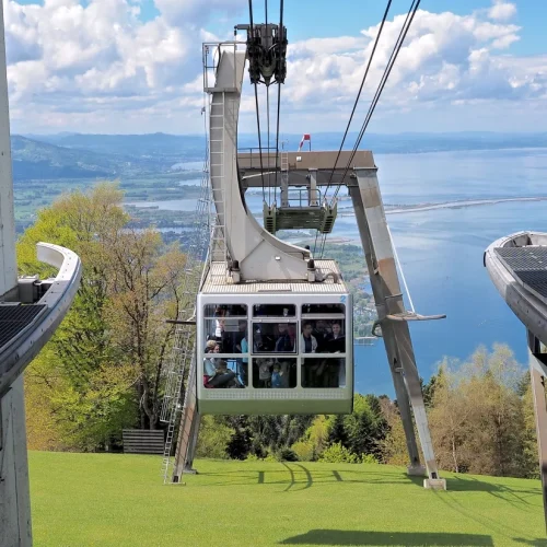 Seilbahn über grüne Landschaft und See.